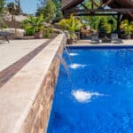 outdoor living space with in ground swimming pool, water falls, water feature, patio, pavers, pavilion, fire pit, natural stone stairs, and retaining walls