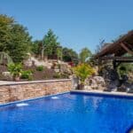 outdoor living space with in ground swimming pool, water falls, water feature, patio, pavers, pavilion, fire pit, natural stone stairs, and retaining walls