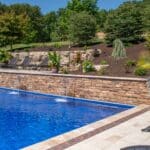 outdoor living space with in ground swimming pool, water falls, water feature, patio, pavers, pavilion, fire pit, natural stone stairs, and retaining walls