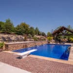 outdoor living space with in ground swimming pool, water falls, water feature, patio, pavers, pavilion, fire pit, natural stone stairs, and retaining walls