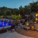 outdoor living space with in ground swimming pool, water falls, water feature, patio, pavers, pavilion, fire pit, natural stone stairs, and retaining walls