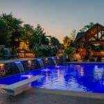 outdoor living space with in ground swimming pool, water falls, water feature, patio, pavers, pavilion, fire pit, natural stone stairs, and retaining walls