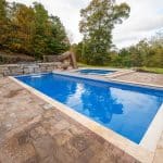 fiberglass swimming pool with paver patio, retaining wall, hot tub, and water slide with landscaping beds