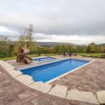 fiberglass swimming pool with paver patio, retaining wall, hot tub, and water slide with landscaping beds