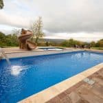 fiberglass swimming pool with paver patio, retaining wall, hot tub, and water slide with landscaping beds
