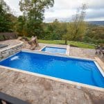 fiberglass swimming pool with paver patio, retaining wall, hot tub, and water slide with landscaping beds