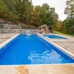 fiberglass swimming pool with paver patio, retaining wall, hot tub, and water slide with landscaping beds