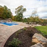 fiberglass swimming pool with paver patio, retaining wall, hot tub, and water slide with landscaping beds