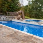 fiberglass swimming pool with paver patio, retaining wall, hot tub, and water slide