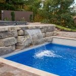 fiberglass swimming pool with paver patio, retaining wall, hot tub, and water slide