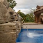 fiberglass swimming pool with paver patio, retaining wall, hot tub, and water slide