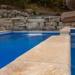 fiberglass swimming pool with paver patio, retaining wall, hot tub, and water slide