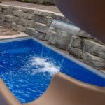 fiberglass swimming pool with paver patio, retaining wall, hot tub, and water slide