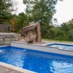 fiberglass swimming pool with paver patio, retaining wall, hot tub, and water slide