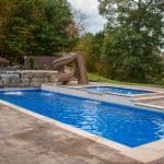 fiberglass swimming pool with paver patio, retaining wall, hot tub, and water slide