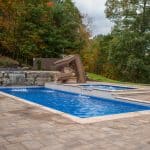 fiberglass swimming pool with paver patio, retaining wall, hot tub, and water slide