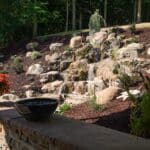 large waterfall and water feature on a steep hill side with landscaping and mountain boulders with flagstone paver landing