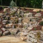 large waterfall and water feature on a steep hill side with landscaping and mountain boulders with flagstone paver landing