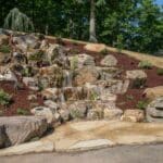 large waterfall and water feature on a steep hill side with landscaping and mountain boulders with flagstone paver landing