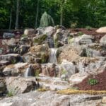 large waterfall and water feature on a steep hill side with landscaping and mountain boulders with flagstone paver landing