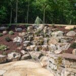 large waterfall and water feature on a steep hill side with landscaping and mountain boulders with flagstone paver landing