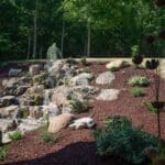 large waterfall and water feature on a steep hill side with landscaping and mountain boulders