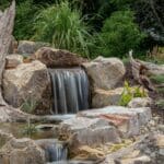 water feature with waterfall, mountain boulders, and landscaping