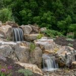 water feature with waterfall, mountain boulders, and landscaping