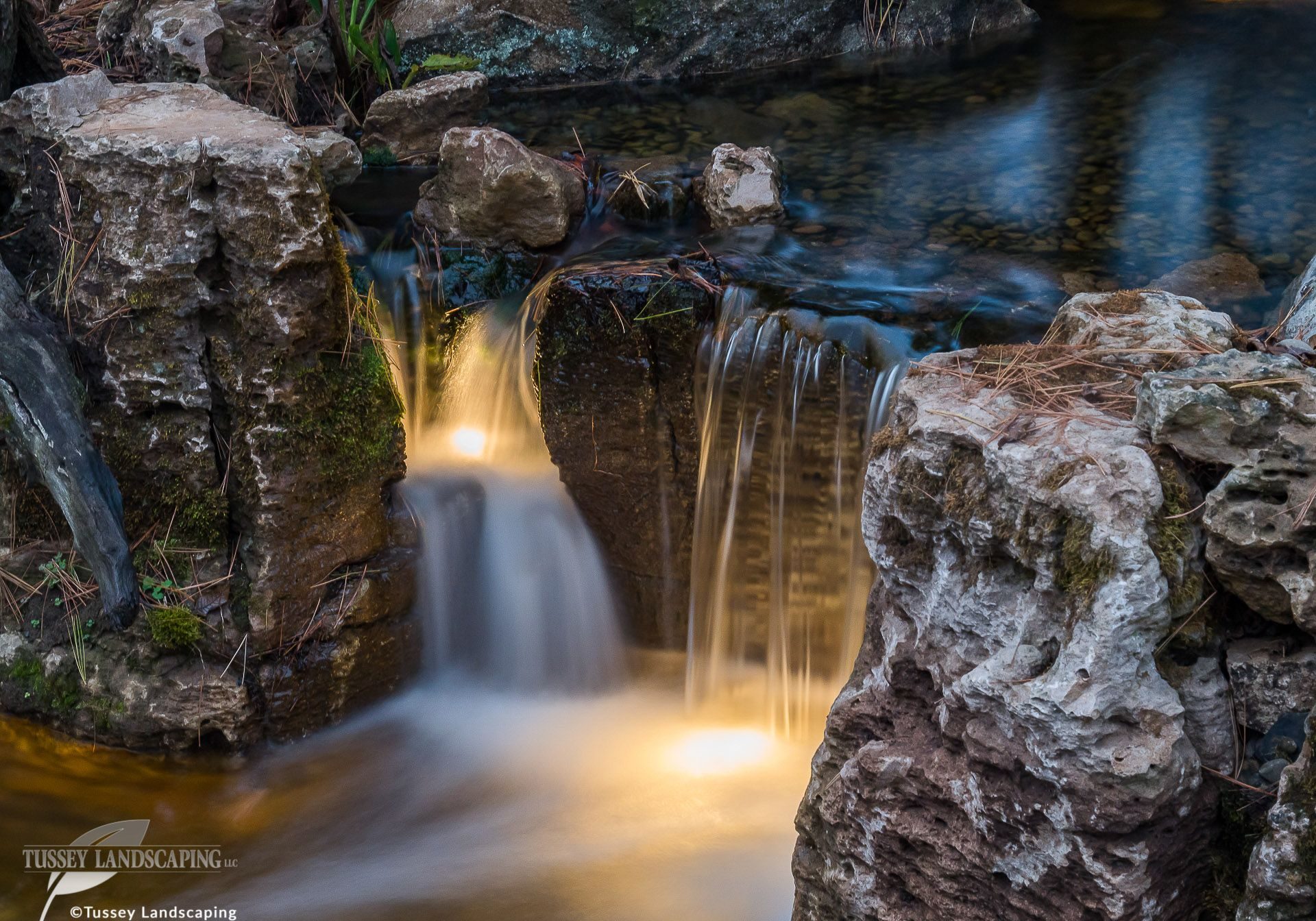 A waterfall in a pond with rocks in the background.