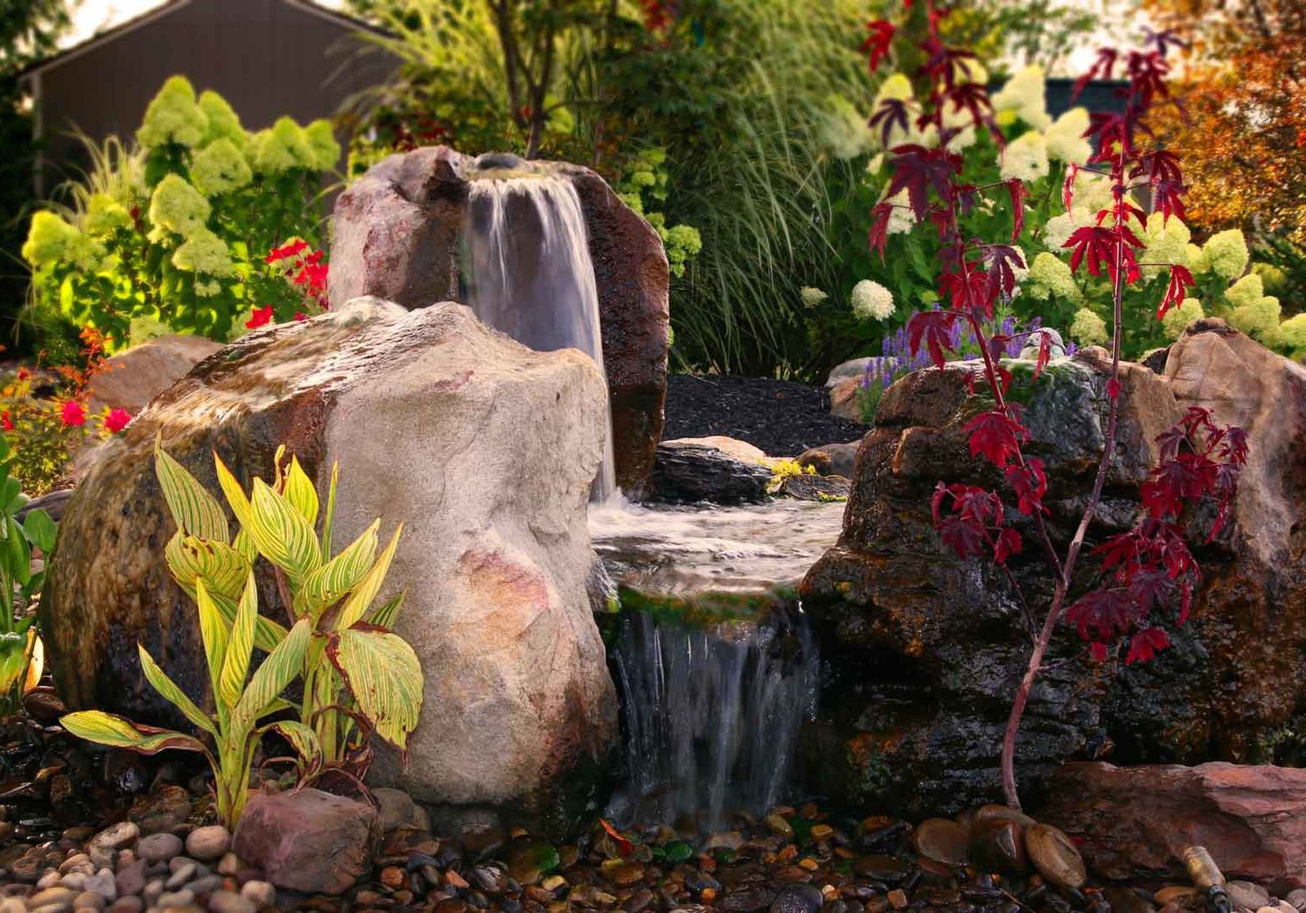 A waterfall in a garden with rocks and plants.