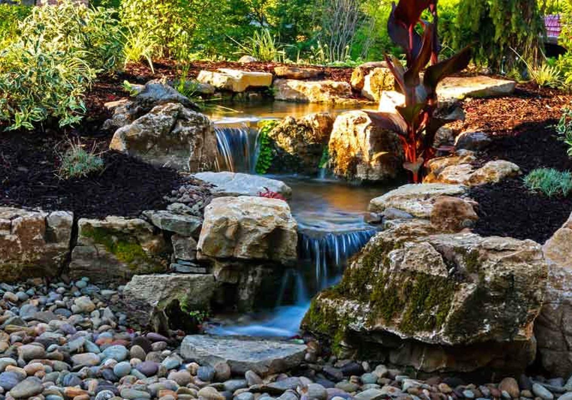 A waterfall in a garden with rocks and plants.