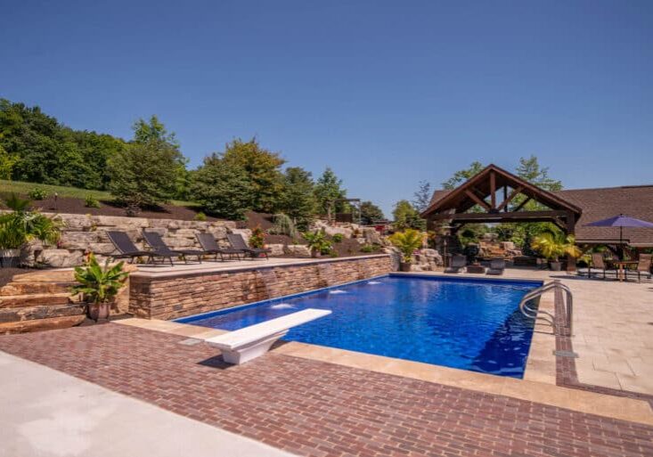 outdoor living space with in ground swimming pool, water falls, water feature, patio, pavers, pavilion, fire pit, natural stone stairs, and retaining walls