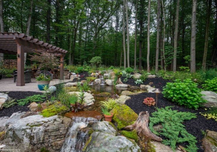pergola on paver patio with natural stone stairs, landscaping, and mountain boulders