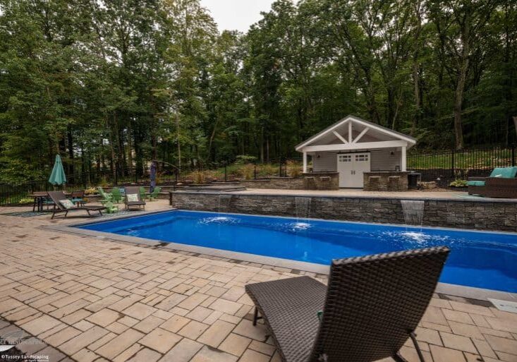 Fiberglass swimming pool with spillway paver patio and pool house and outdoor living space