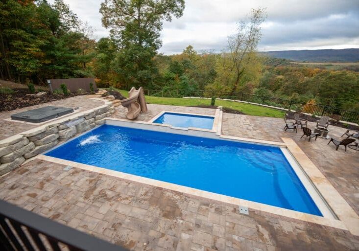 fiberglass swimming pool with paver patio, retaining wall, hot tub, and water slide with landscaping beds