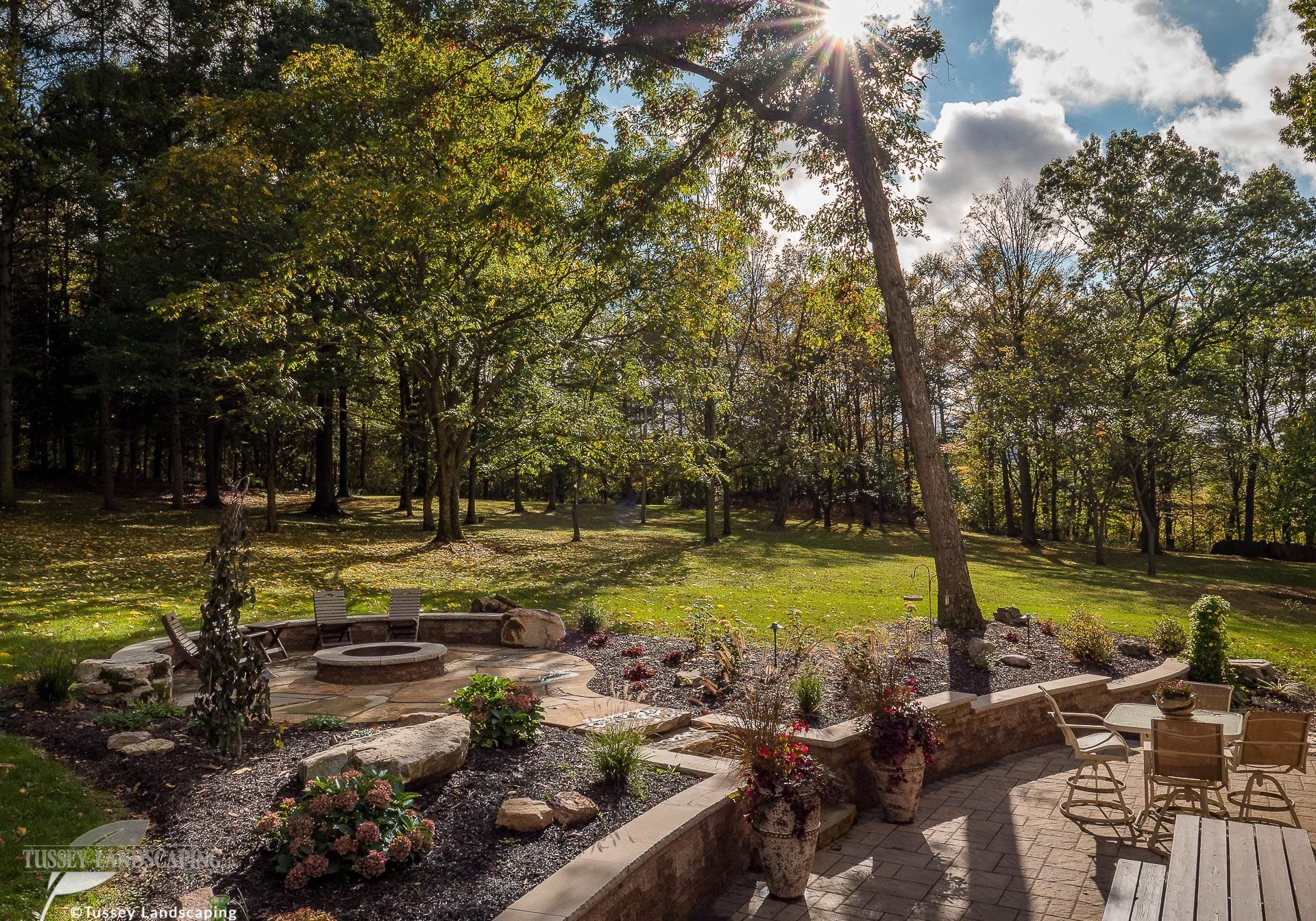 A stone patio with a fire pit in the middle of a wooded area.