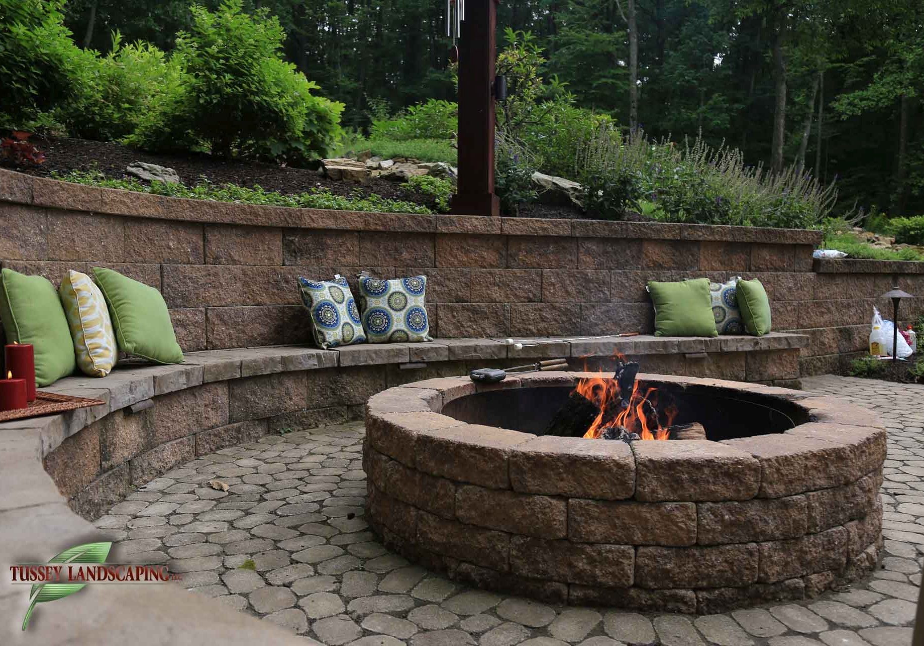 A patio with a fire pit and green pillows.