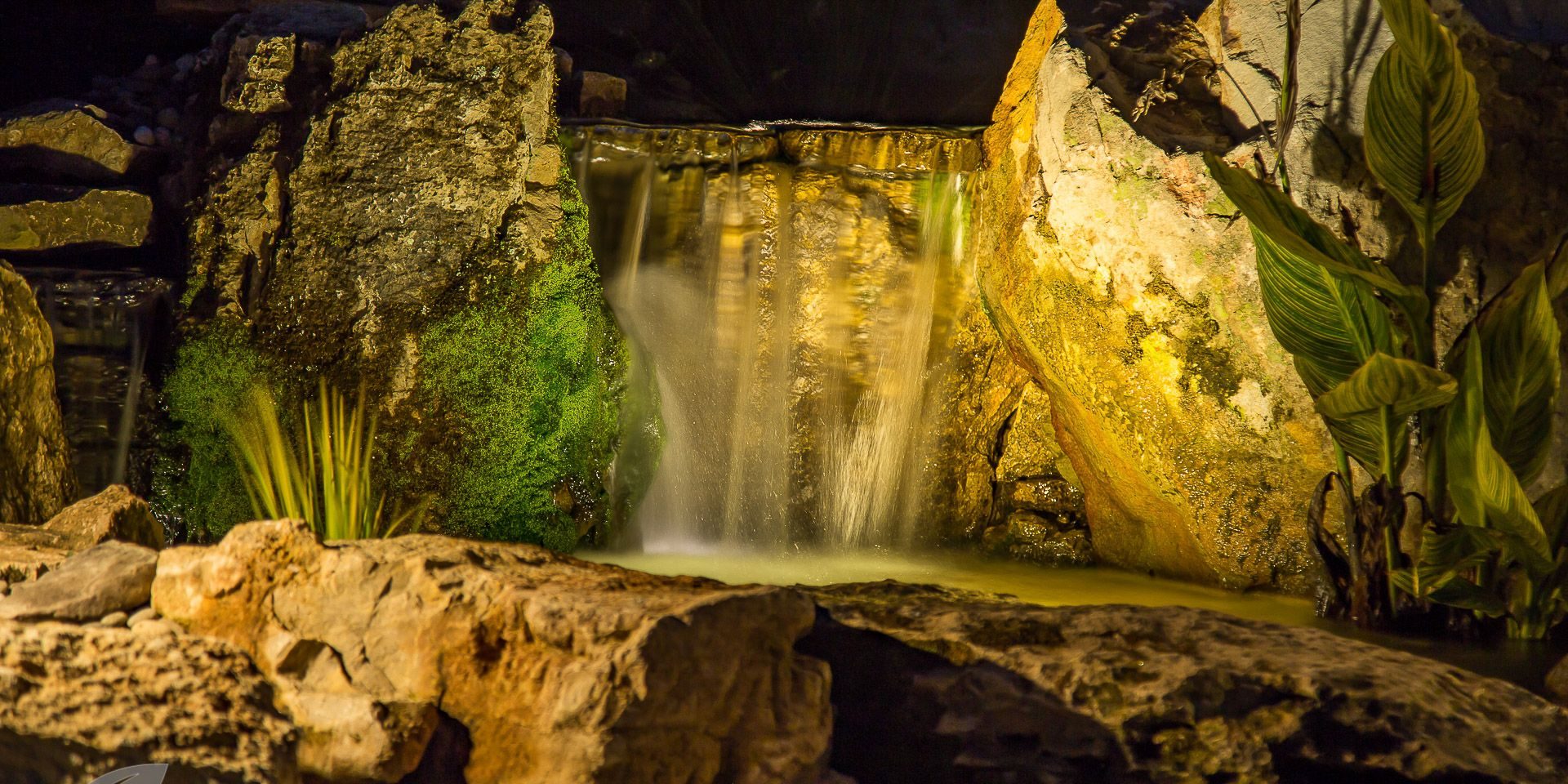 lighting24 A waterfall in the middle of a rock garden at night.