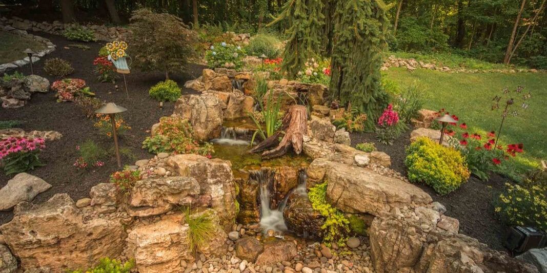 A rock waterfall in a garden surrounded by trees.