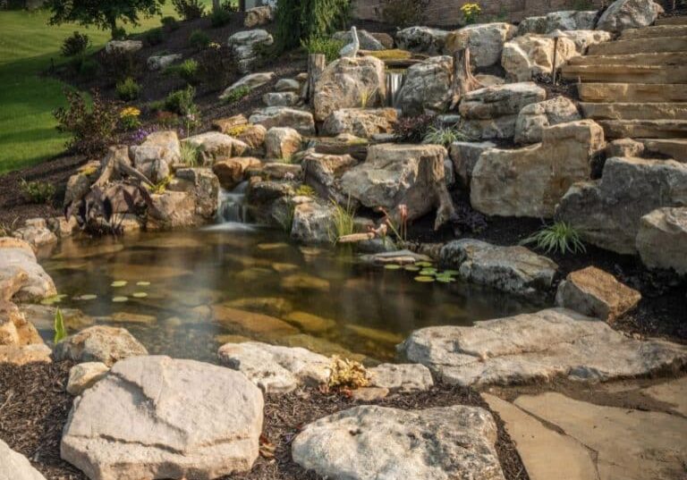 pond with mountain boulders and stream beside a flagstone patio