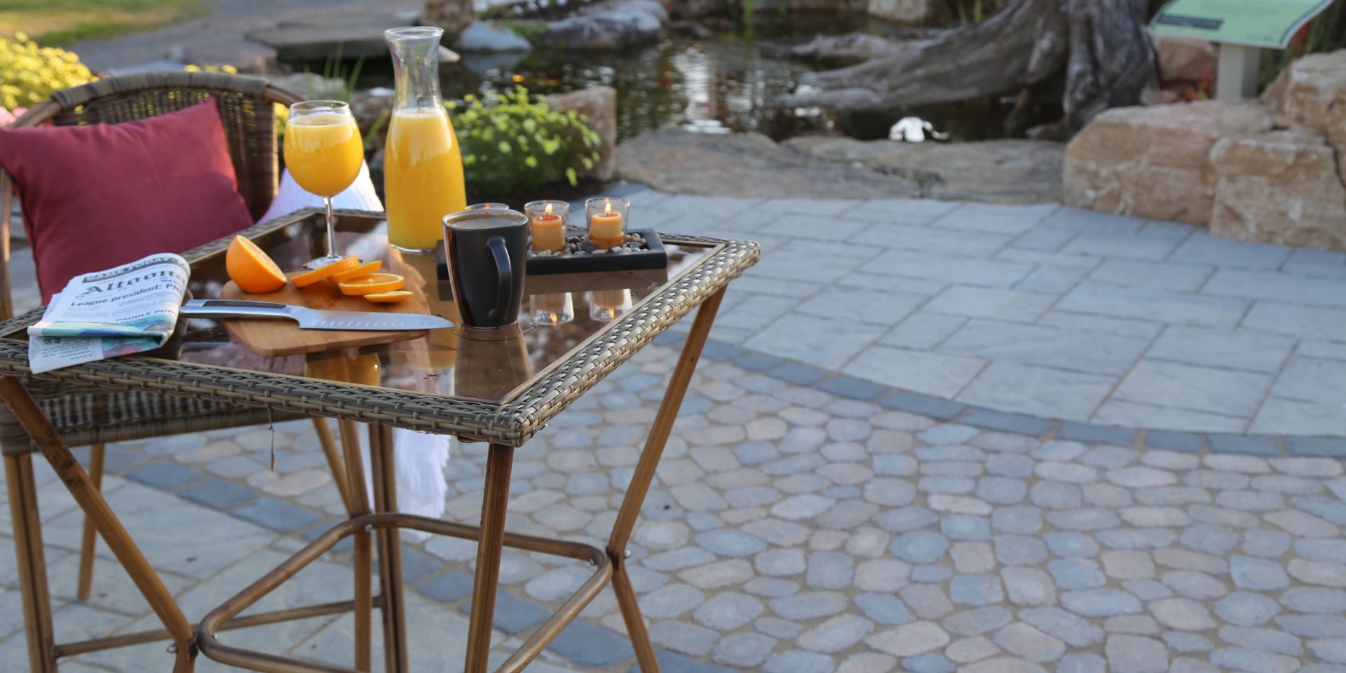 A table with a cup of orange juice and a wicker chair.